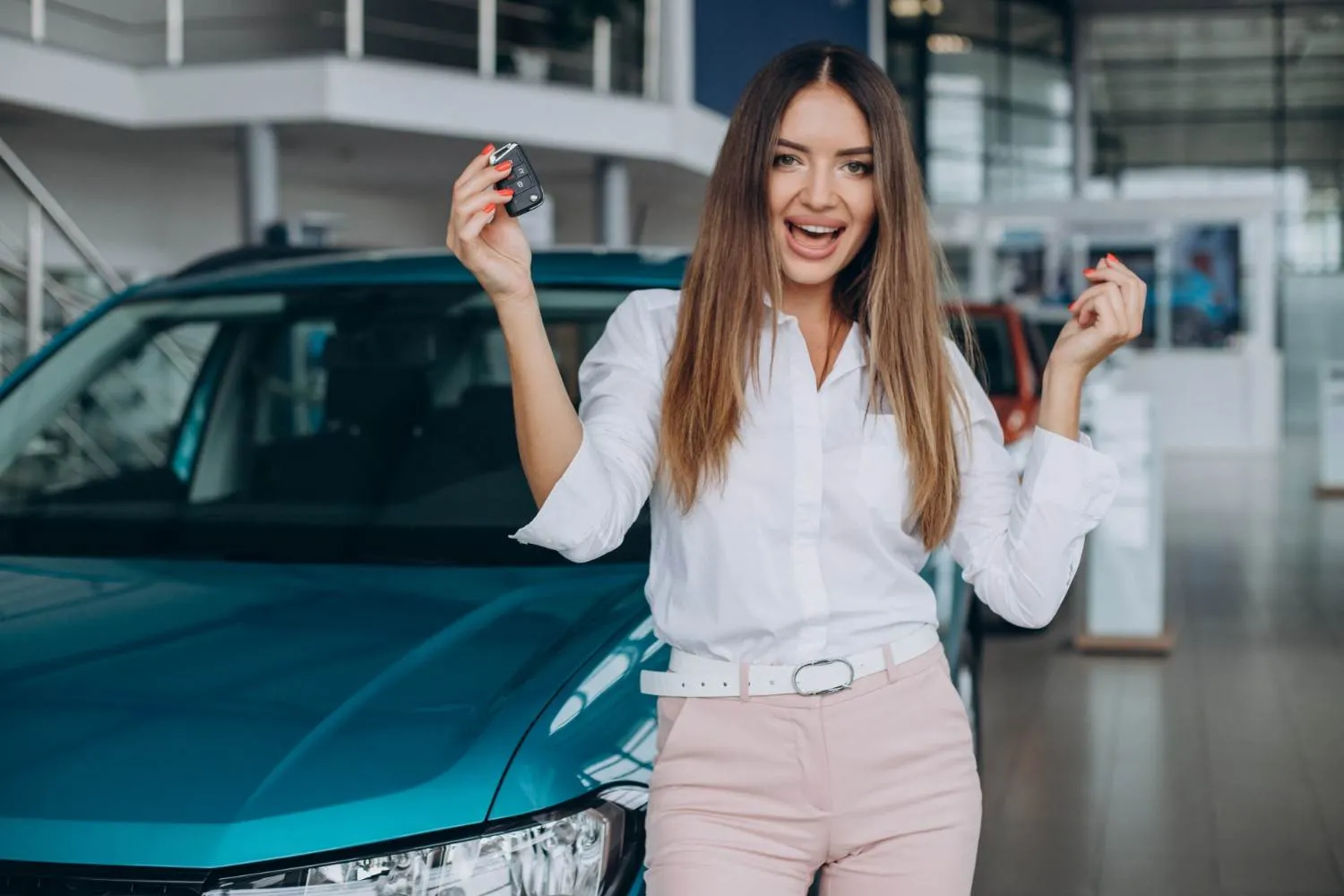 A smiling driver holding up a car key beside a teal car